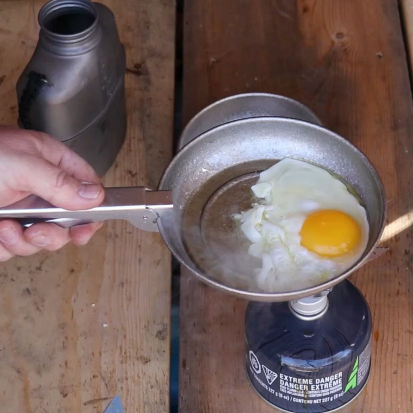 SilverAnt Titanium Camping Plate with a Crystallized Finish 400ml/13.53 fl oz - in use image - frying an egg with the pot gripper on a stove