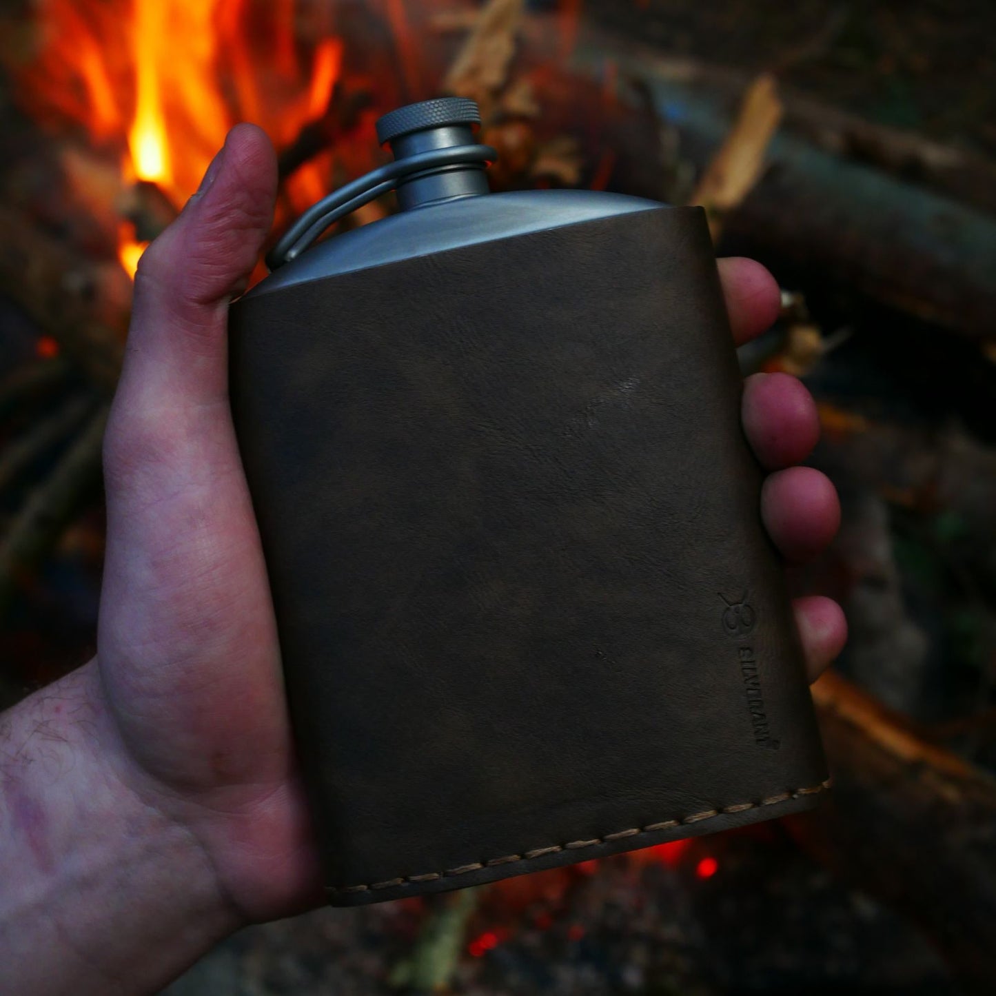 
                  
                    Titanium Hip Flask With Funnel - 220ml/7.74 fl oz - with Pu leather - held in a hand  in front of a campfire
                  
                
