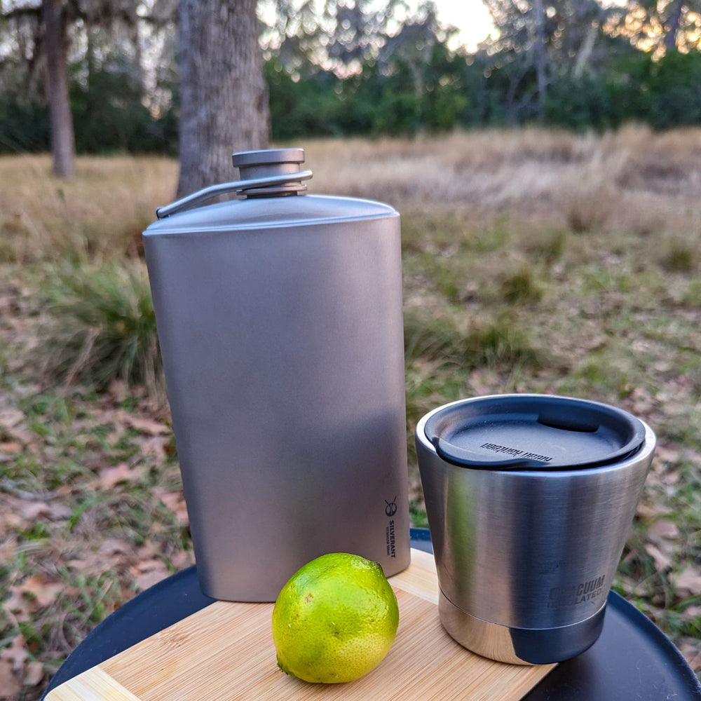 
                  
                    Large Titanium Hip Flask & Funnel 500ml/17.59 fl oz - sandblasted finish - on a cutting board with a cup and a lemon
                  
                