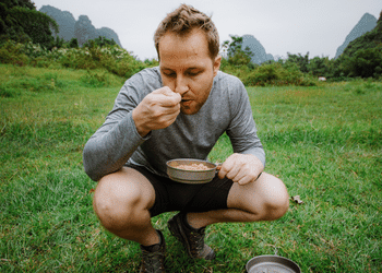SilverAnt Outdoors Man Crouched Eating with a Titanium Spoon Holding A Titanium Frying Pan