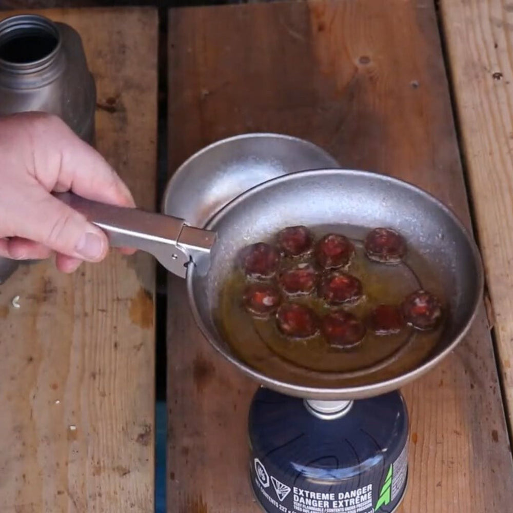 
                  
                    SilverAnt Titanium Camping Plate with a Crystallized Finish 400ml/13.53 fl oz - in use image - frying sausage with the pot gripper on a stove
                  
                