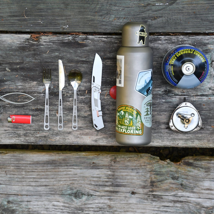 
                  
                    SilverAnt Ultralight Large Titanium Water Bottle With Titanium Cup - In-Use (Actual product photo, laid on top of old wooden outdoors camping table with various other essential camp gear)
                  
                