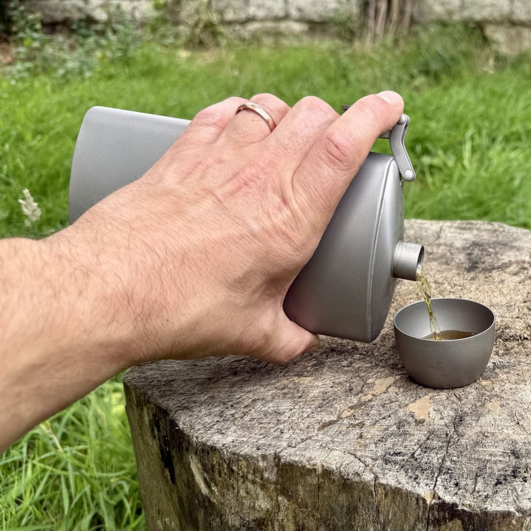 
                  
                    SilverAnt Ultralight Titanium Hip Flask 450ml/15.22 fl oz & Shot Glasses - Actual product photo, in use, on hand, pouring a drink into shot glass on a wooden stump
                  
                