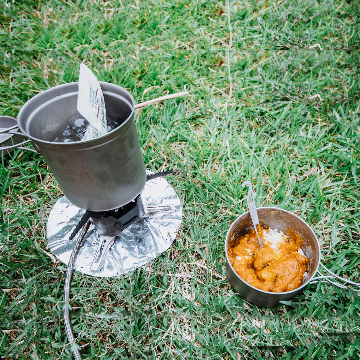 SilverAnt Ultralight Titanium Spork with Bottle Opener - actual product photo, on a titanium pot with foldable handle, cooking food pack at the side, eating curry with rice
