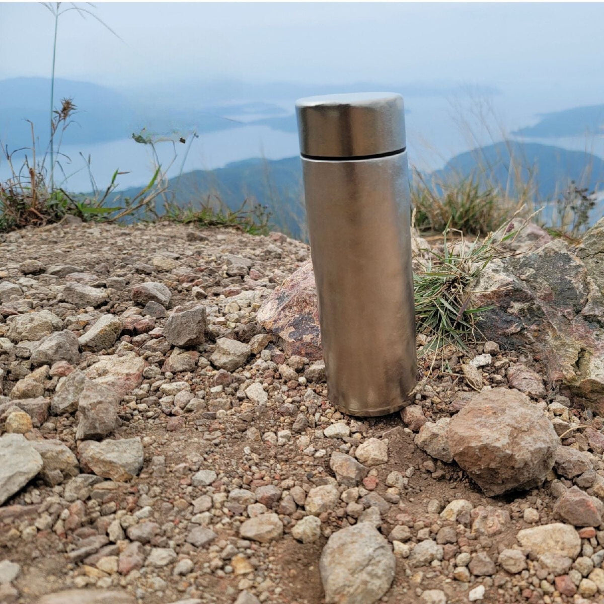 Titanium Double-Wall Insulated Thermos Flask 400ml/14fl oz - actual product photo, crystallized, lifestyle photo, placed on a high cliff overlooking a beautiful mountain view