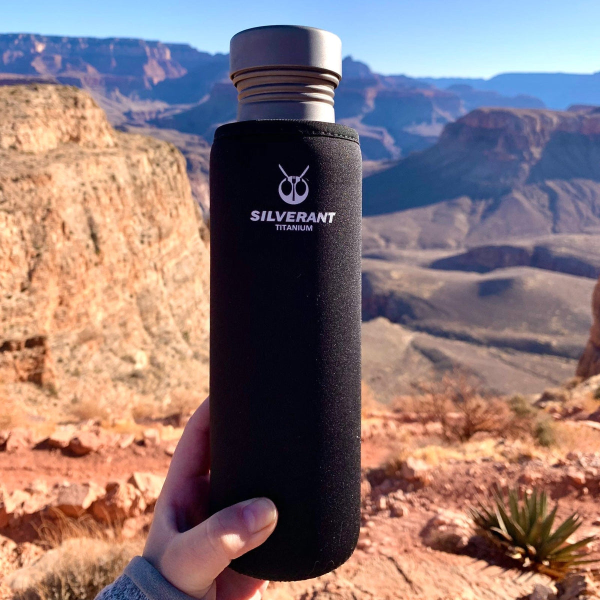 SilverAnt Ultralight Round Titanium Water Bottle - In-Use (on-hand, black thermal sleeve, grand canyon in the background, silverant branding, actual product photo)
