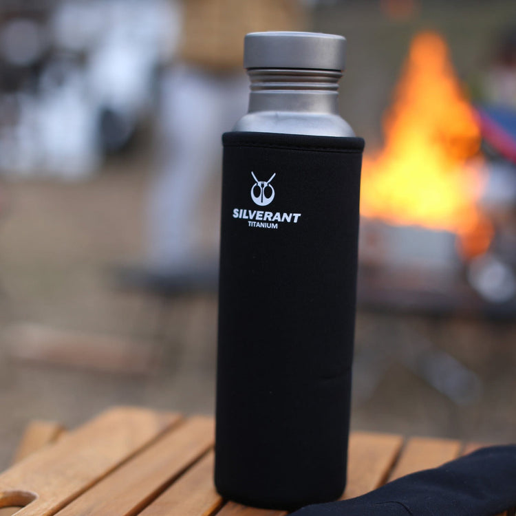 
                  
                    SilverAnt Ultralight Round Titanium Water Bottle - 800ml - In-Use (black thermal sleeve, actual product photo, lifestyle shot, placed on top of wooden camping table with blurry background)
                  
                