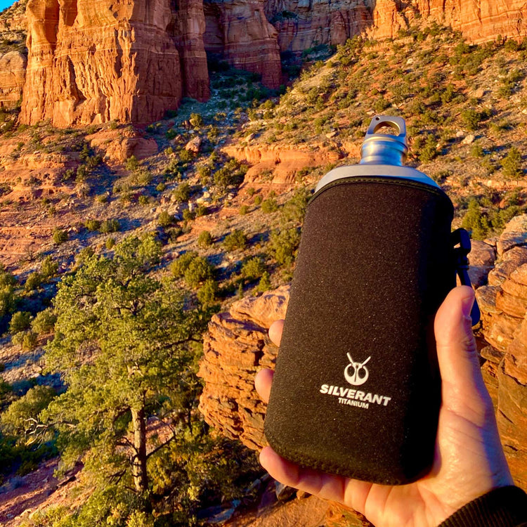
                  
                    SilverAnt Ultralight Titanium Water Bottle 800ml/28.16 fl oz (Slim Sandblasted) - In-Use (held in front of beautiful cliff view, thermal sleeve, silverant branding)
                  
                