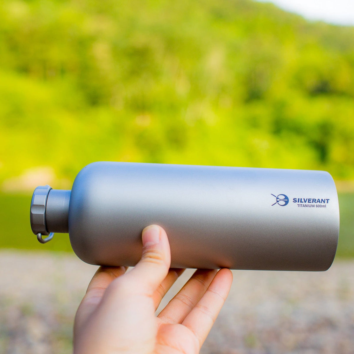 SilverAnt Ultralight Titanium Water Bottle Narrow Mouth Design - 600ml/21.1 fl (actual product photo, lifestyle shot, on-hand, holding bottle out on its side, outdoors)